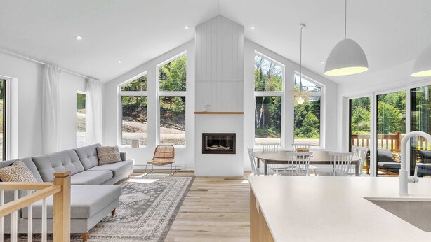 A spacious living area with a fireplace, large windows, a dining table, and a kitchen island. - Spa, Mountain and River | Le Zenith (Saint-Côme)