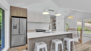 A modern kitchen with a stainless steel refrigerator, white cabinetry, a wooden countertop, and a bar stool area. - Spa, Mountain and River | Le Zenith (Saint-Côme)