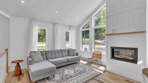 A modern living room with a grey sectional sofa, a patterned rug, and a fireplace. - Spa, Mountain and River | Le Zenith (Saint-Côme)