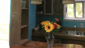 Een keuken met blauwgroene wanden, houten planken, een houten aanrecht, een vaas met bloemen en twee hanglampen.