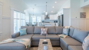 A modern living room with a grey sectional sofa, a coffee table, and a dining area in the background. - Rooftop Sunsets • Ocean Glimpse • Sleeps 10 (Ocean City)