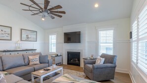 A spacious living room with a fireplace, a ceiling fan, and a television mounted on the wall. - Rooftop Sunsets • Ocean Glimpse • Sleeps 10 (Ocean City)