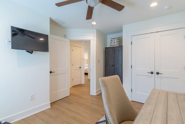 A room with a ceiling fan, a flat-screen TV mounted on the wall, a dining table with chairs, and a wardrobe. - Rooftop Sunsets • Ocean Glimpse • Sleeps 10 (Ocean City)