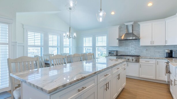 A modern kitchen with white cabinetry, a large island with marble countertop, and a central range hood. - Rooftop Sunsets • Ocean Glimpse • Sleeps 10 (Ocean City)