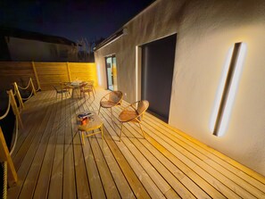 Una terraza de madera con mobiliario exterior, una mesa de vidrio y sillas.