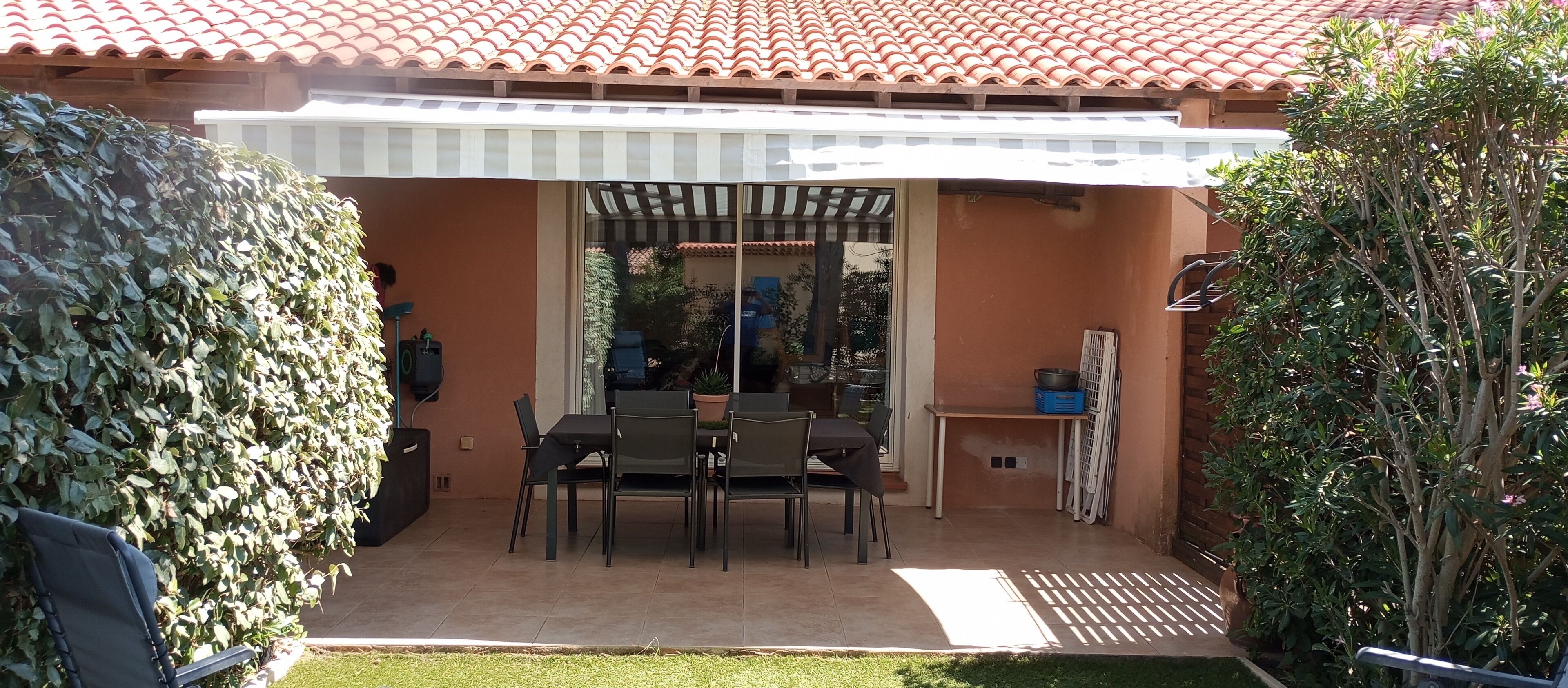 A patio with a table and chairs, a white awning, and a potted plant.