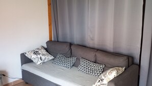 Een grijze bank met patroon kussens, een grijze gordijn en een witte stoel in een kamer met een betegelde vloer.