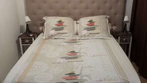 Een netjes opgemaakt bed met een bloemenbedekking, twee kussens met een motief van stenen, en een nachtkastje met een lamp.