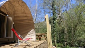 A wooden deck with a covered area, a red chair, and a wooden railing. - ZEcamping toboggans piscine animaux acceptés locatif 16m2 4 pers (Saint-Constant-Fournoulès)