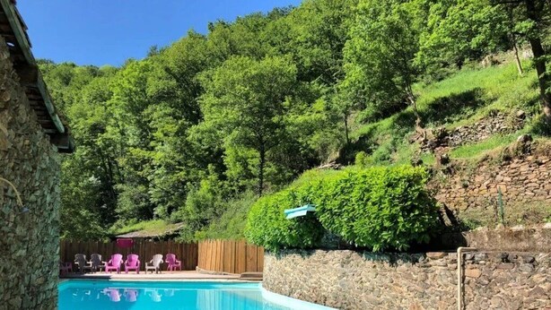A swimming pool surrounded by stone walls, with a wooden deck and chairs in the background. - ZEcamping toboggans piscine animaux acceptés locatif 16m2 4 pers (Saint-Constant-Fournoulès)