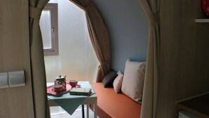 A cozy room with a bed, a table with a kettle and cups, and a window. - ZEcamping toboggans piscine animaux acceptés locatif 16m2 4 pers (Saint-Constant-Fournoulès)