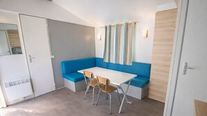 Een kleine kamer met een witte tafel, twee stoelen, een blauwe bank en een raam met gestreepte gordijnen.