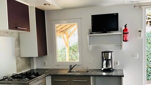 A compact kitchen with a gas stove, a sink, and a coffee maker. - ZEcamping 3 étoiles piscine chauffée mobil-home TV clim 33m2 6 pers (Portel-des-Corbières)
