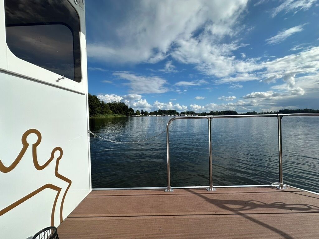 A boat with a metal railing and a view of a calm lake with trees in the background.