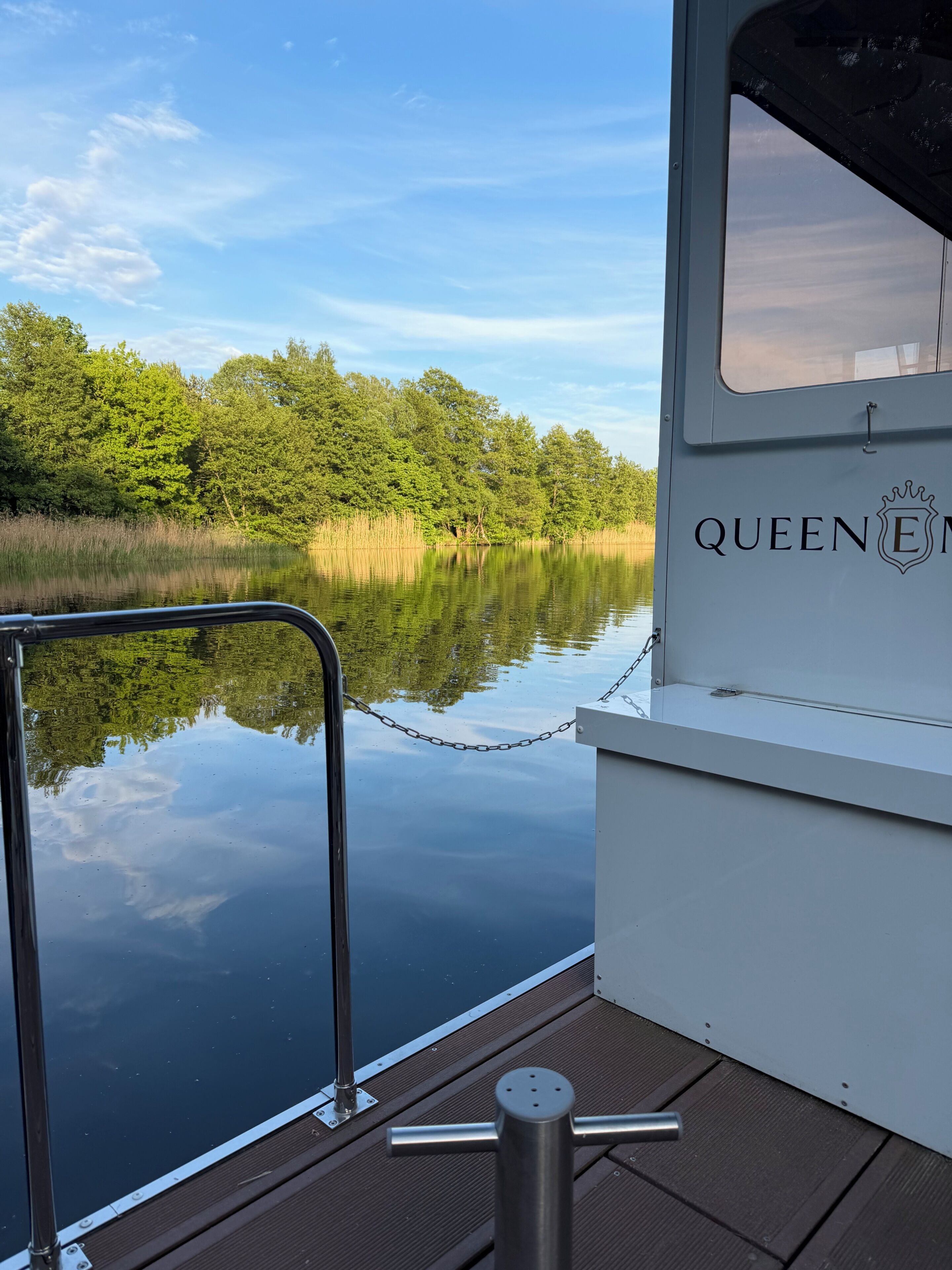 A boat with 'QUEEN EM' on the side, calm water, and a forested shoreline.