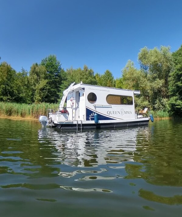 A houseboat named 'Queen Emma' with a small deck and a circular window, floating on a calm river surrounded by greenery. - The Queen Emma Houseboat! Deep relaxation on gentle waves!!! (Zehdenick)