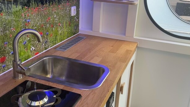 A compact kitchenette with a gas stove, stainless steel sink, and a window overlooking a garden. - Houseboat Queen Emma! Deep relaxation on gently rocking waves!!! (Zehdenick)