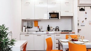 Una cocina moderna con armarios blancos, un lavamanos de acero inoxidable y un horno. Hay una mesa de comedor con sillas naranjas y un mantel blanco.