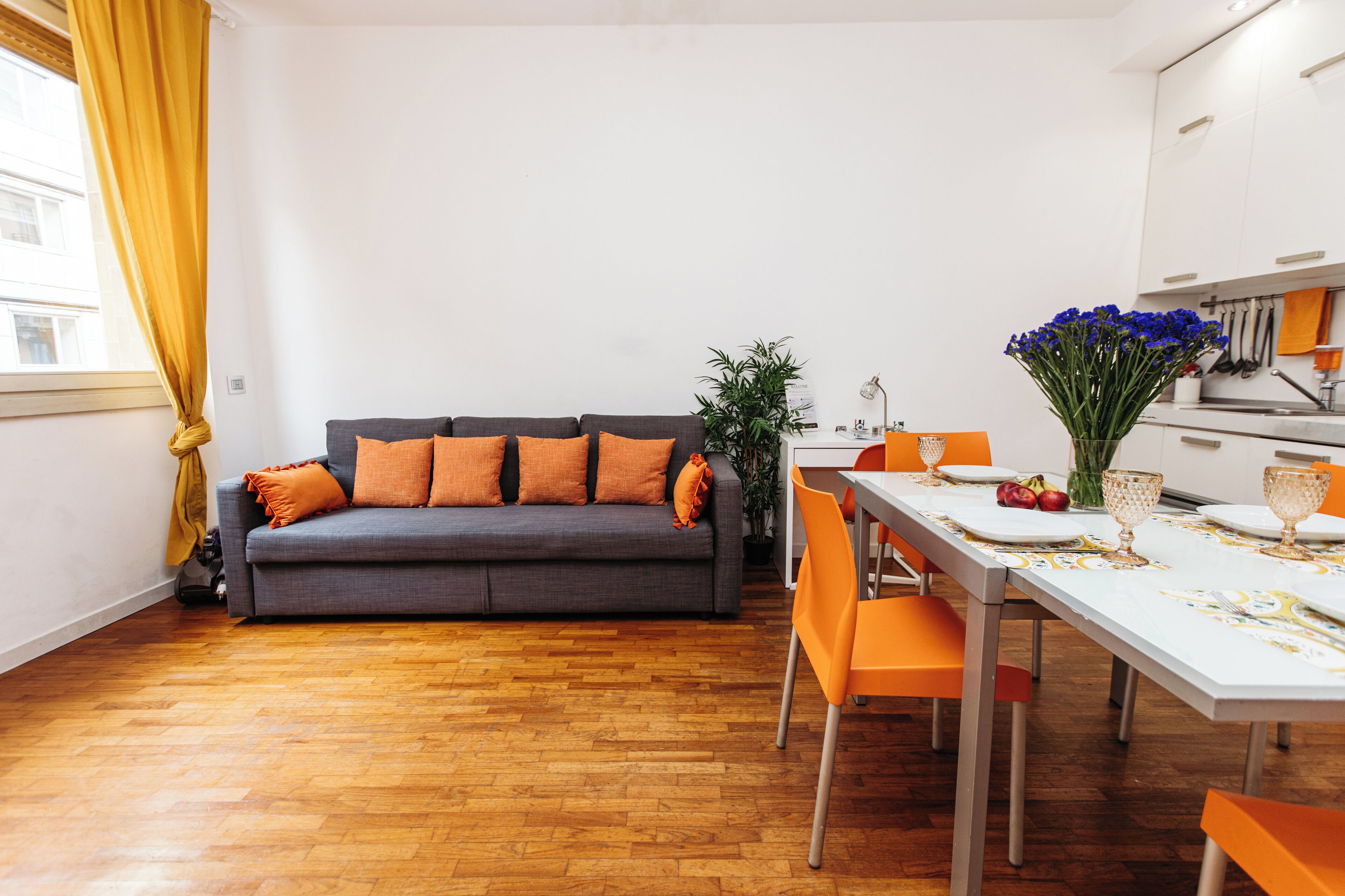 Un salon moderne avec un canapé gris, des coussins orange et une table à manger assortie de chaises orange.