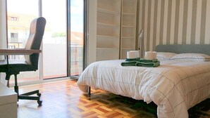 Habitación de hotel con cama, una silla, un escritorio y vistas a través de una puerta corrediza de vidrio.