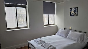 A bedroom with a bed, two windows, and artwork on the walls.