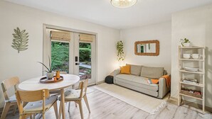 Ein modernes Wohnzimmer mit einem runden Esstisch, Holzstühlen, einem grauen Sofa, einem weißen Bücherregal und einer hängenden Pflanze.