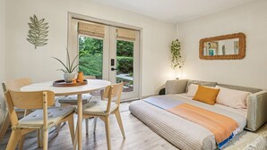 Ein Zimmer mit einem Bett, einem Esstisch mit Stühlen, einer Pflanze und einem Fenster mit Jalousien.