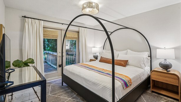 Ein Himmelbett mit Baldachin, ein Nachttisch mit Lampe und Blick auf einen Balkon mit Holzgeländer.