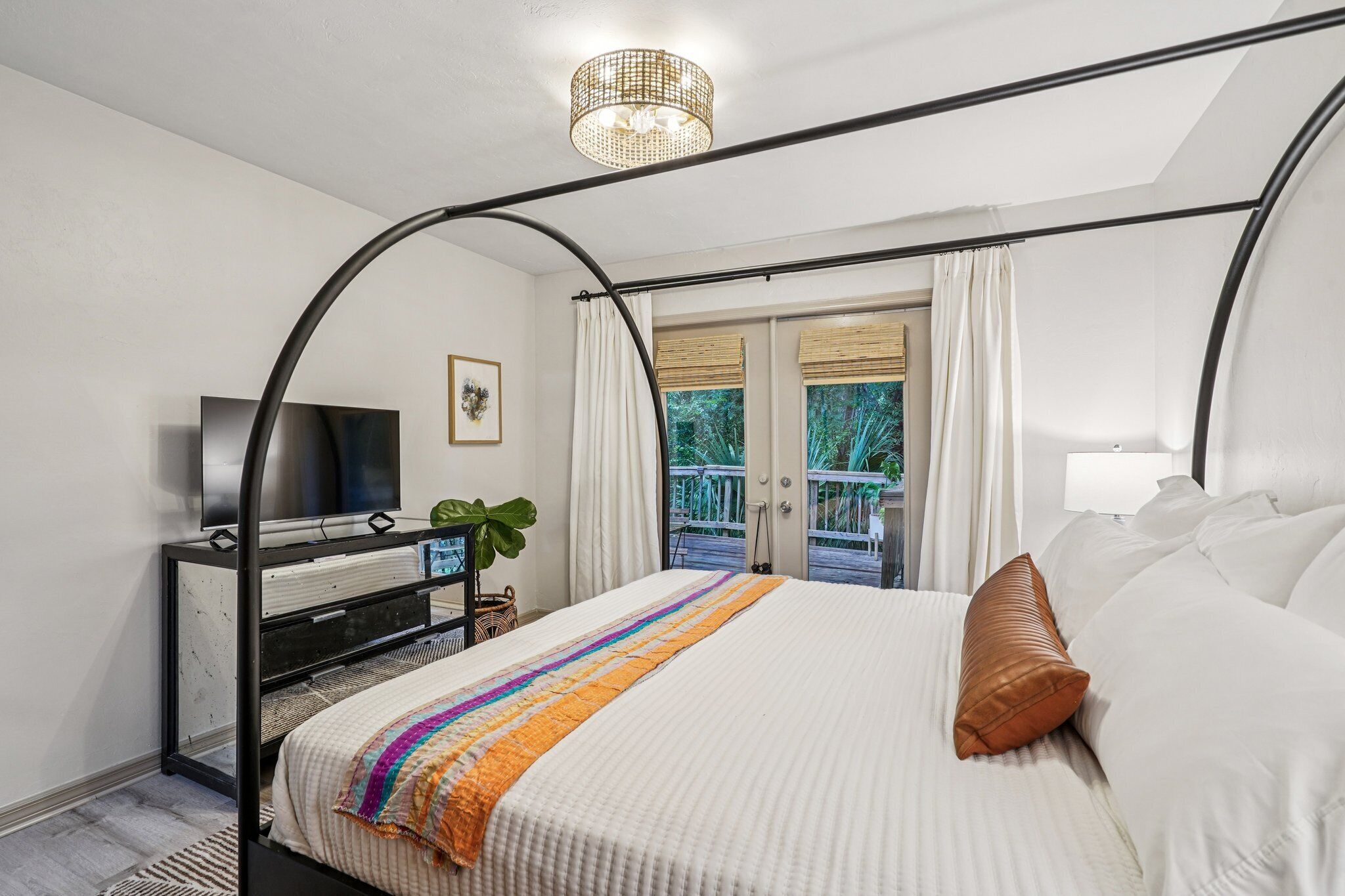 A bedroom with a bed, a TV, a plant, and a balcony with curtains.