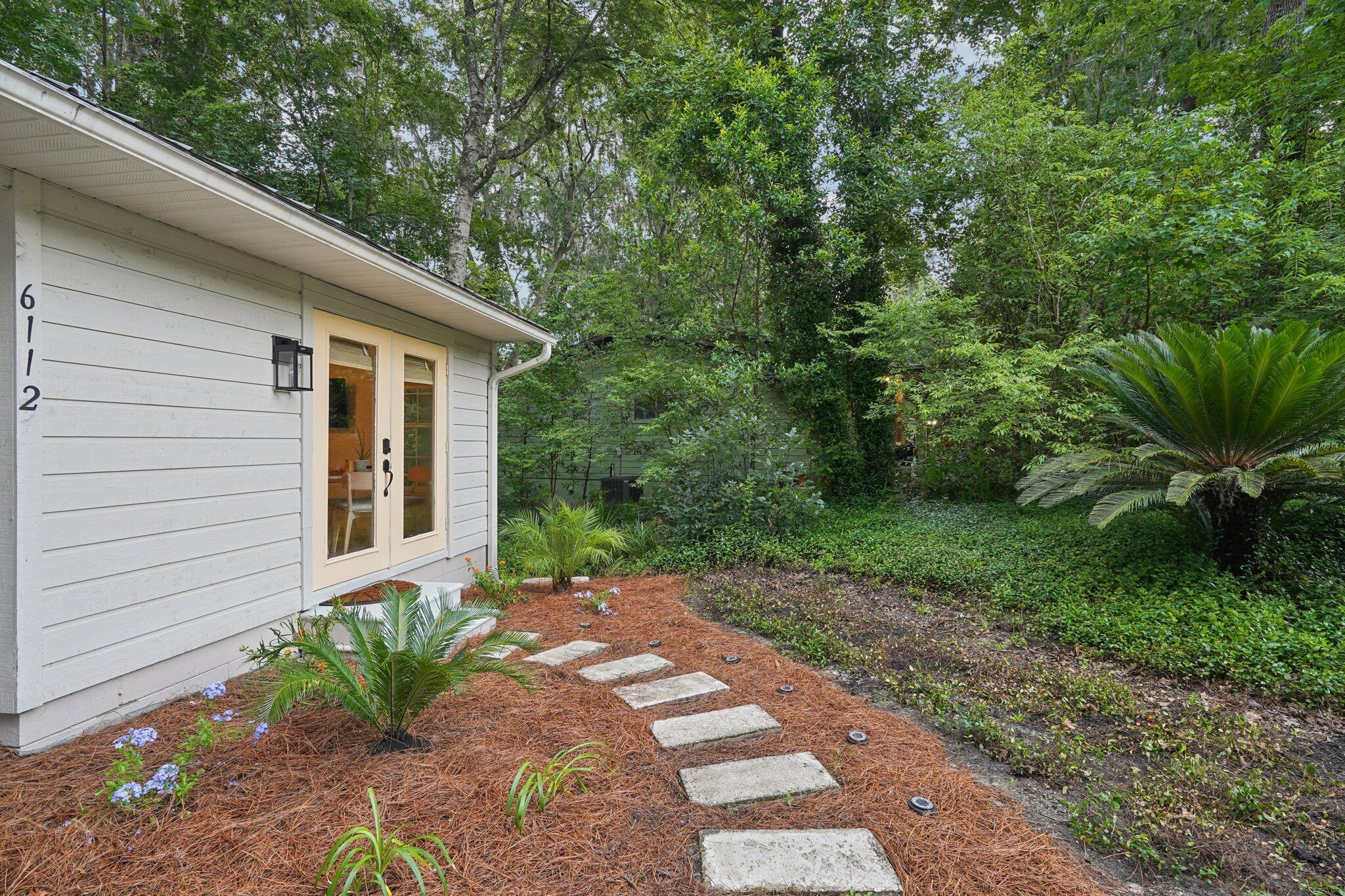 A house with a number 612 on the side, surrounded by a garden with stepping stones and various plants.