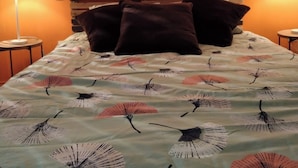 Una cama con colcha estampada con flores, dos lámparas de noche y un cuadro de un paisaje urbano en la pared.
