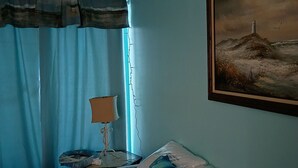 Ein Schlafzimmer mit Bett, Lampe, Gemälde und Vorhängen.