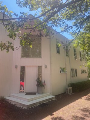 Un edificio de dos pisos con fachada blanca, una puerta principal y un pequeño porche.