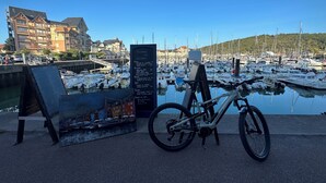 Een fiets geparkeerd in de buurt van een jachthaven, met boten, een bord en een gebouw op de achtergrond.
