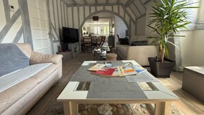 Een woonkamer met een hoge plafond, zichtbare balken, een bank, een bijzettafeltje met tijdschriften, een televisie en een potplant.