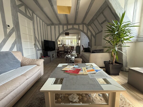 A living room with a high ceiling, exposed beams, a sofa, a coffee table with magazines, a television, and a potted plant.