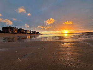 A beach with a sunset, buildings in the background, and a calm sea.