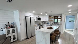 Een moderne keuken met witte kastjes, een marmeren eiland en een zithoek met krukken.