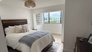 Een slaapkamer met een bed, een raam, een dressoir en een plafondlamp.