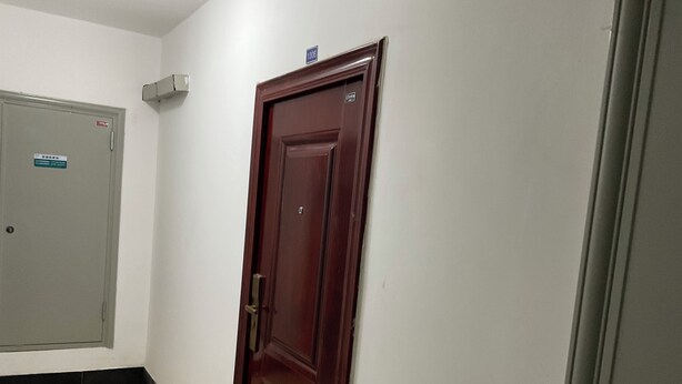 A hallway with a closed wooden door, a grey door with a sign, and a light switch on the wall. - Marvelous 2-bedroom apartment with WiFi in Yantai (Yantai)