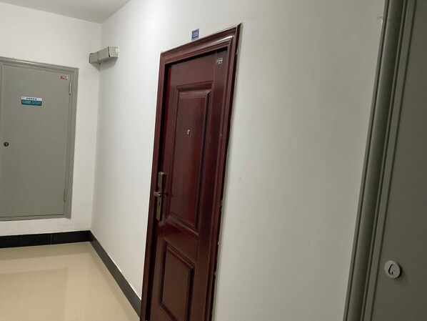 A hallway with a closed wooden door, a grey door with a sign, and a light switch on the wall.