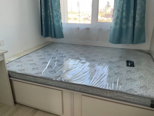 Una habitación con un colchón en el suelo, una mesita y una ventana con cortinas.