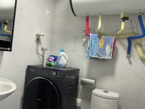 A bathroom with a washing machine, a toilet, a sink, and a towel rack with colorful towels.