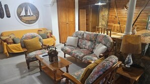 Un salon chaleureux avec un canapé jaune, des fauteuils à motifs floraux, une table basse en bois et un coin repas avec des meubles en bois.