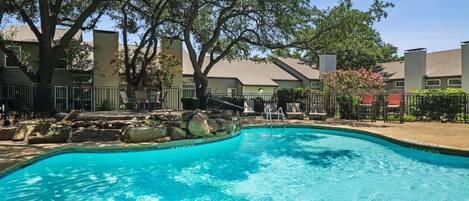 A swimming pool with a stone border, surrounded by lounge chairs and a fence.