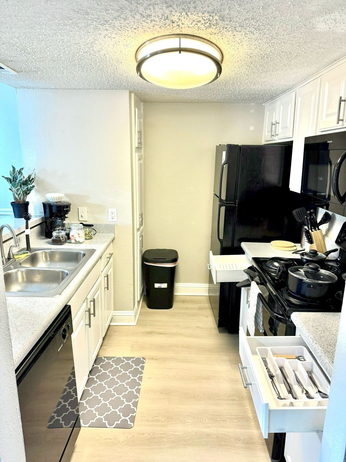 A compact kitchen with a black refrigerator, a stove, a sink, and a trash bin.