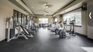 Une salle de sport équipée de divers appareils d’exercice, dotée de grandes fenêtres et d’un ventilateur de plafond.