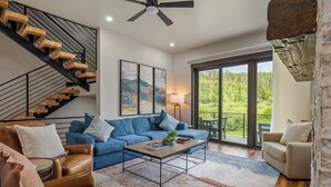 A modern living room with a blue sofa, leather armchairs, a wooden coffee table, and a staircase with wooden steps.