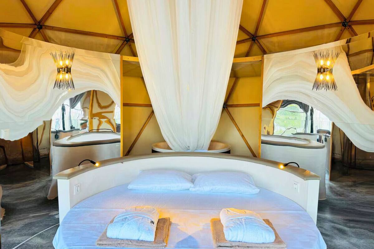 A spacious tent with a large bed, two bedside tables, and a canopy overhead.