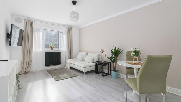 Ein modernes Wohnzimmer mit einem weißen Sofa, einem Esstisch mit Stühlen, einem kleinen Beistelltisch und einer Deckenleuchte.